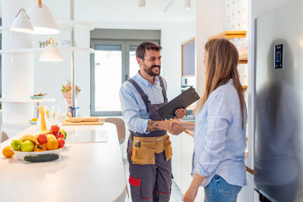 young woman shaking hands to male plumber with clipboard in kitchen room young woman shaking hands to male plumber with clipboard in kitchen room